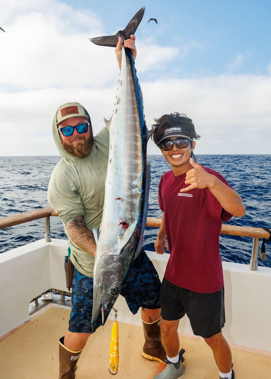 An angler holding up a wahoo next to Richard, a yellow trolling lure hanging from its jaw