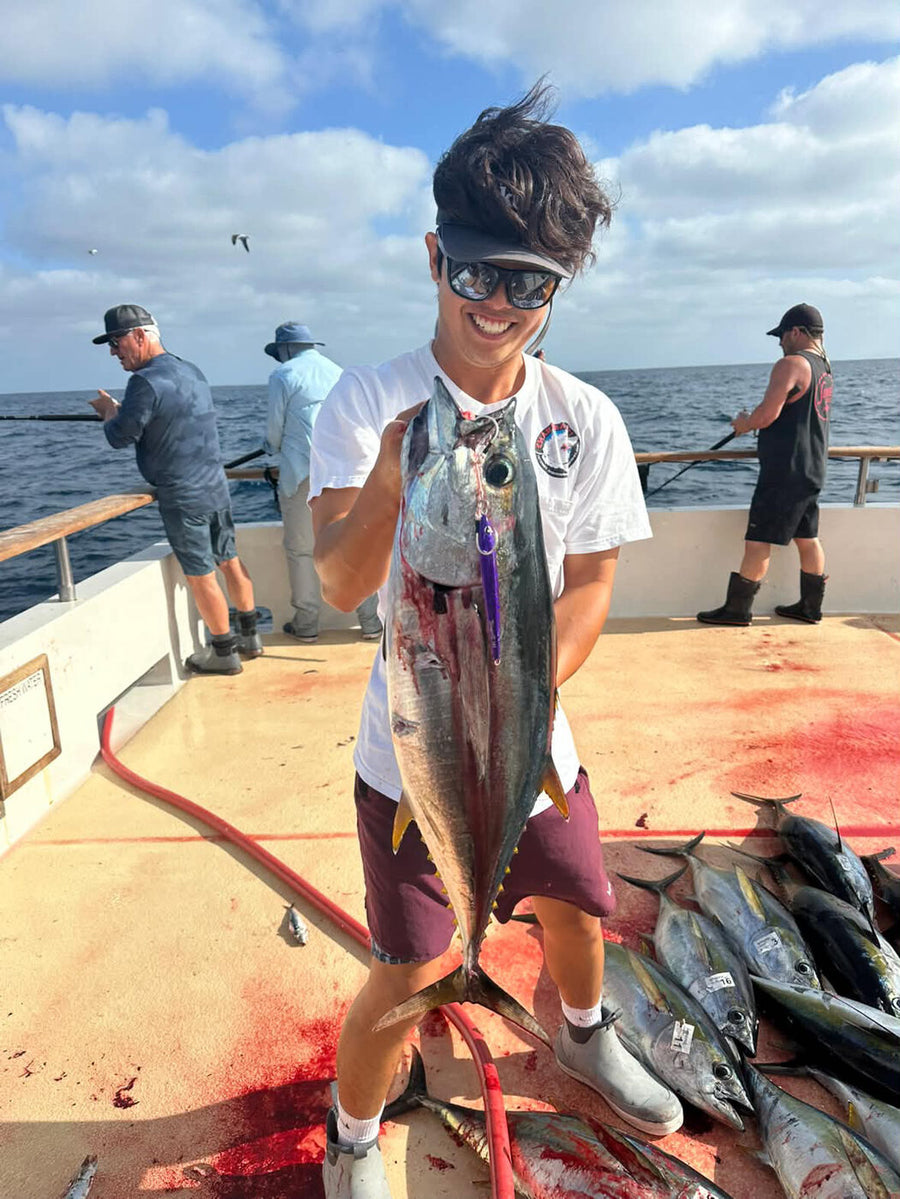 Richard holding a yellowfin tuna with a purple jig in its mouth, more yellowfin on the deck